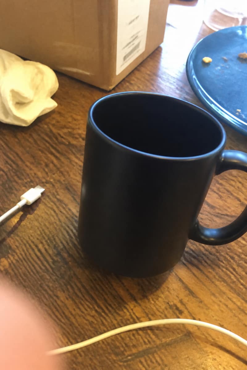 Casual phone photo of a ceramic mug on a messy table, the seller input for this Amazon listing image demo